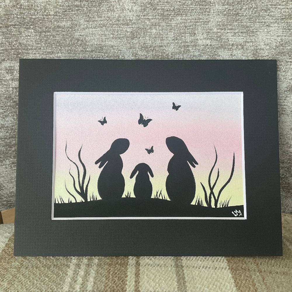 Silhouette artwork of three rabbits and butterflies on a gradient background, framed in black.
