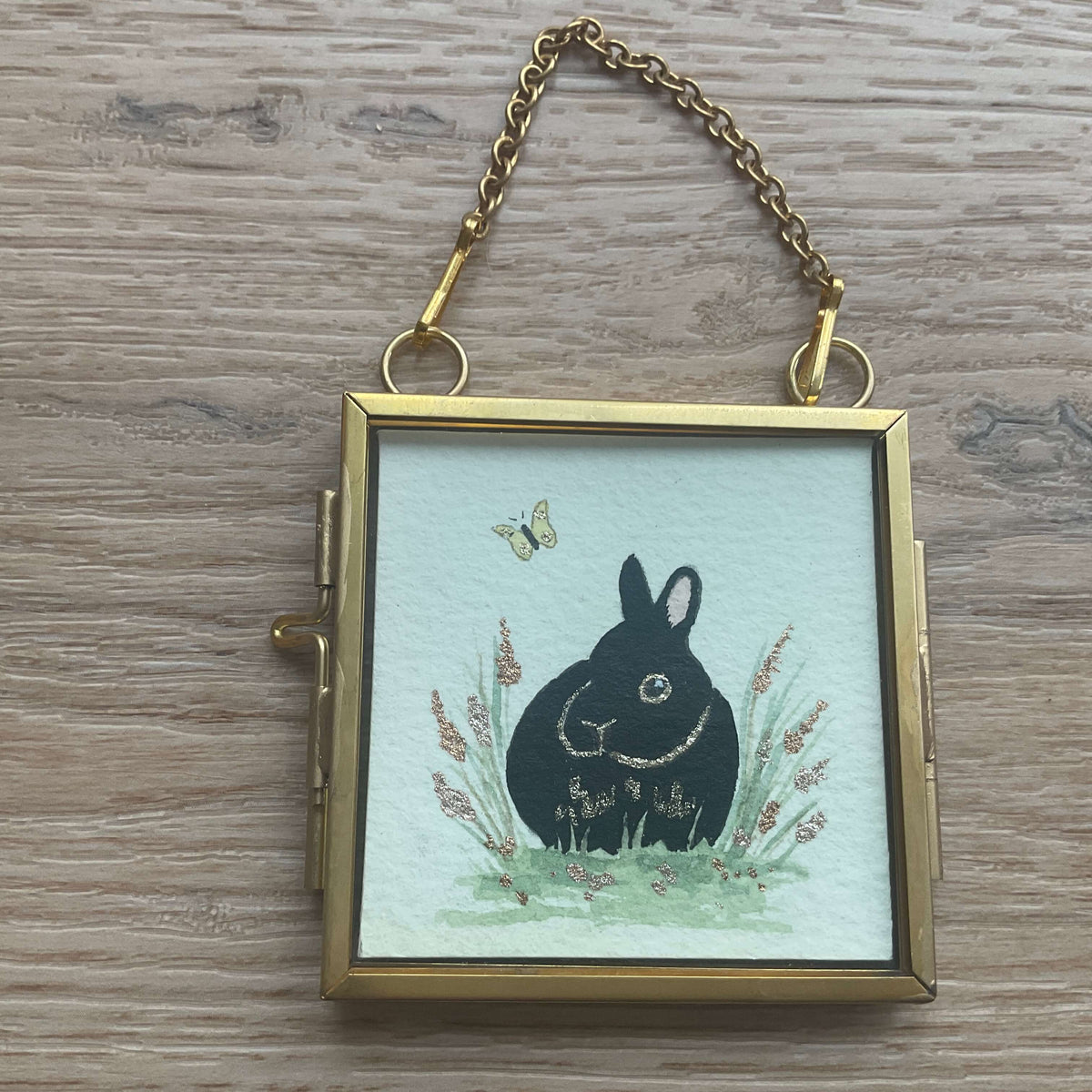 The Gilded Meadow original watercolor painting featuring a black Netherland Dwarf rabbit sitting in vibrant green grass with a yellow butterfly