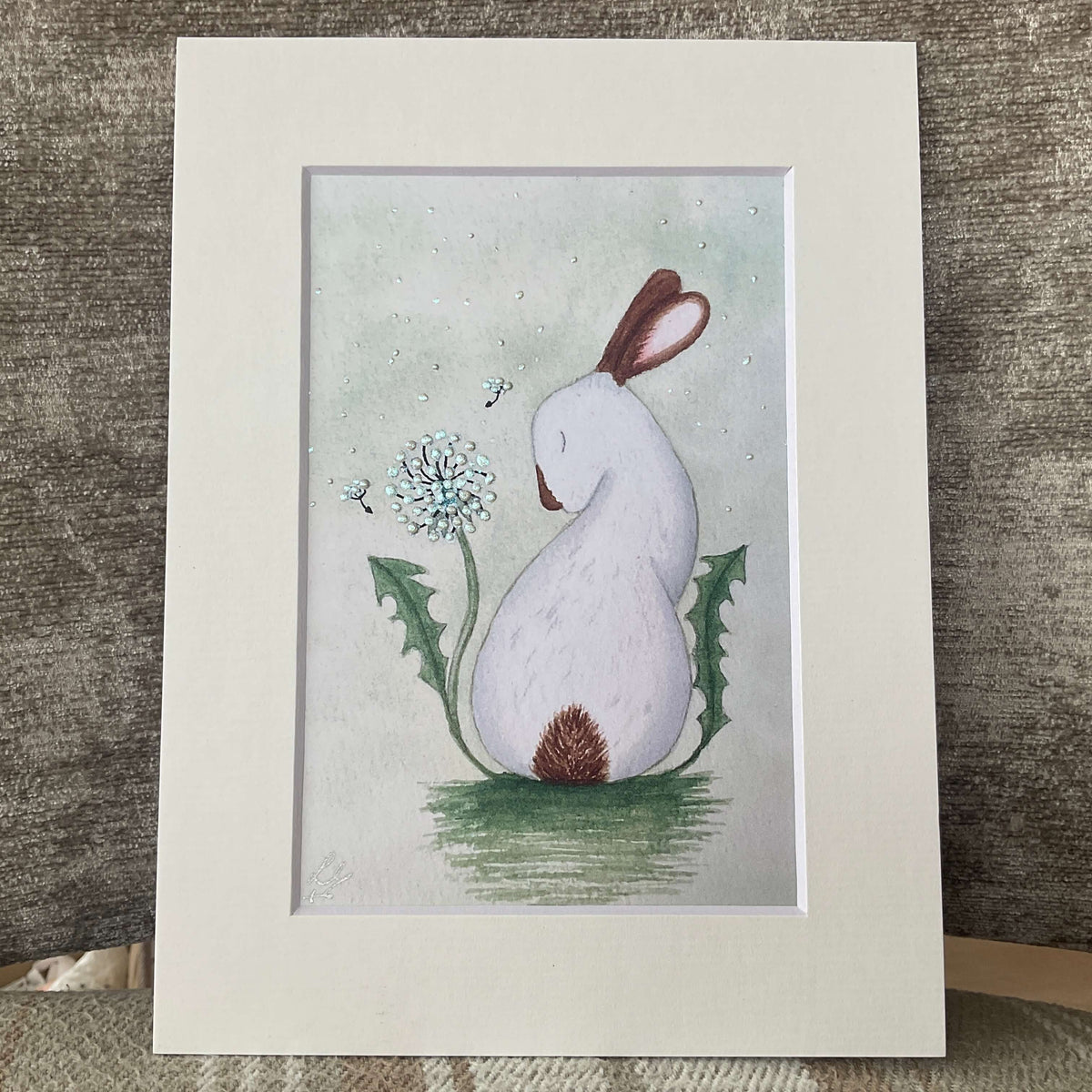 Hand-finished storybook bunny print titled And Every Wish is For You showing a white rabbit with a shimmering iridescent dandelion clock on a sage green background