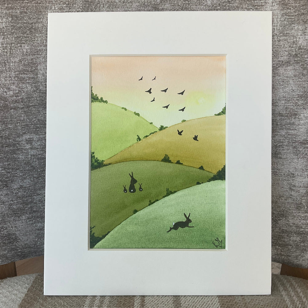 Illustration of rabbits and birds on rolling hills in a white frame.