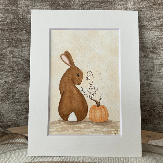 Original watercolor painting titled Autumn Magic featuring a brown rabbit looking at a small spider next to an autumn pumpkin with gold highlights