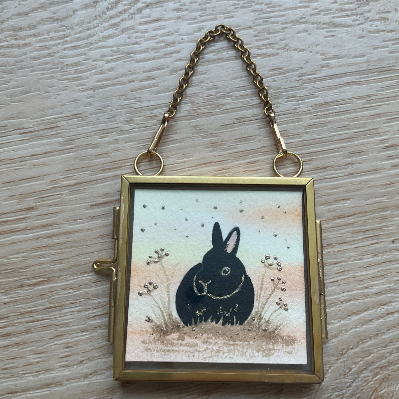 Original mini watercolor painting titled Autumn Whispers featuring a black rabbit silhouette with gold outlines and silver metallic stardust in a hanging metal frame