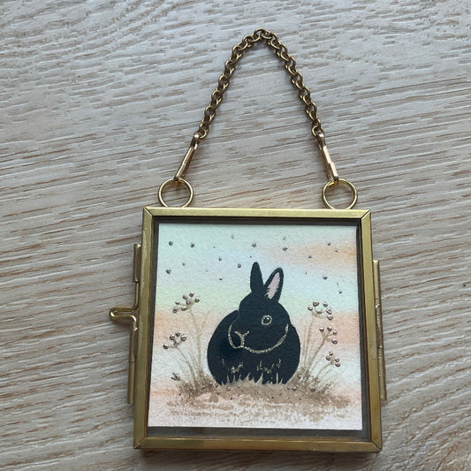 Original mini watercolor painting titled Autumn Whispers featuring a black rabbit silhouette with gold outlines and silver metallic stardust in a hanging metal frame