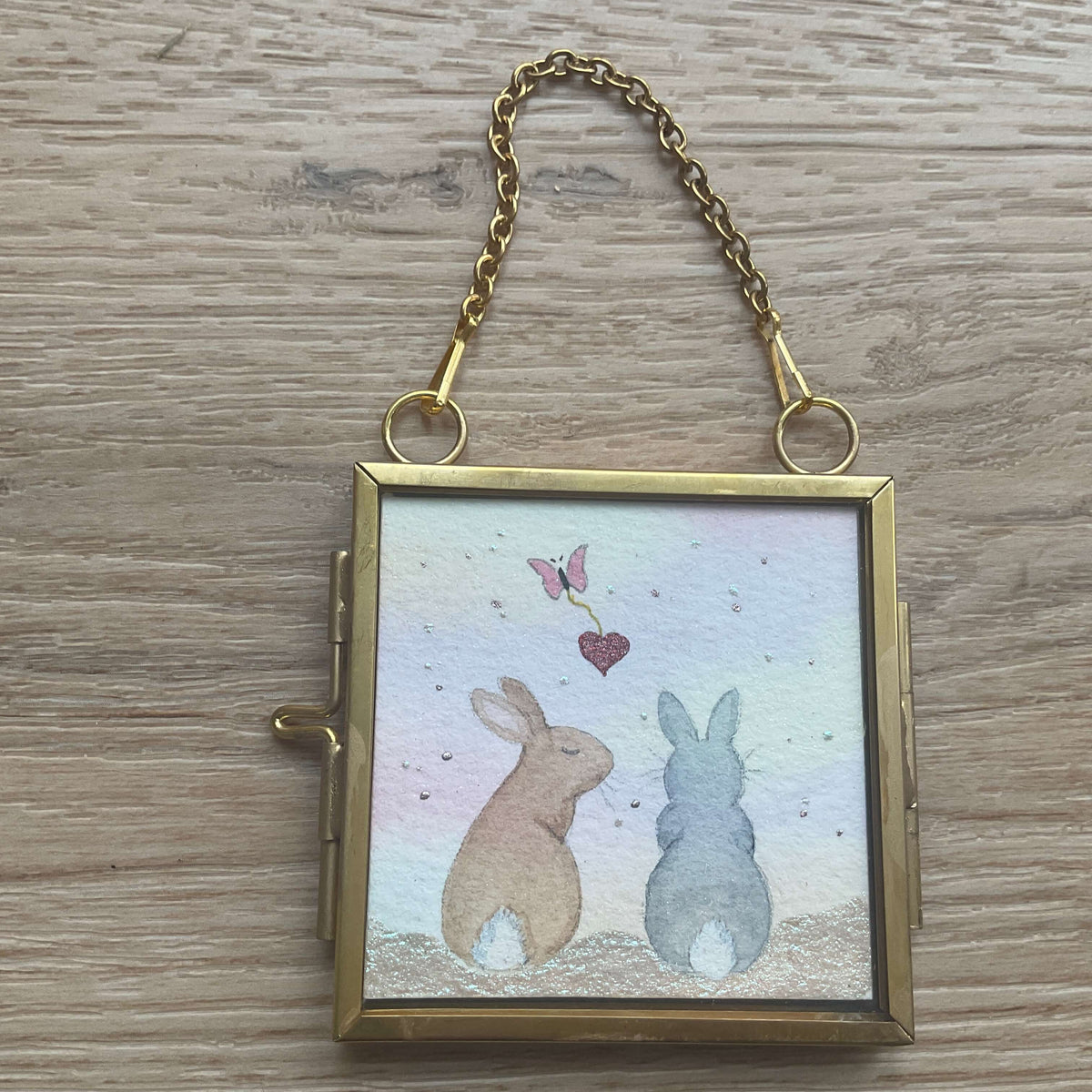 Connected by the Heart pet loss memorial art showing two rabbits sitting together at sunset as a butterfly carries a red heart away.