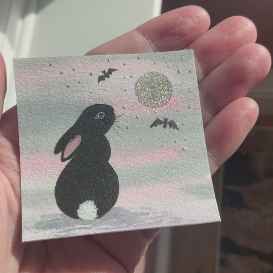 Video of Original mini watercolor painting titled Under the Silver Moon featuring a black rabbit silhouette looking up at a silver metallic moon and bats