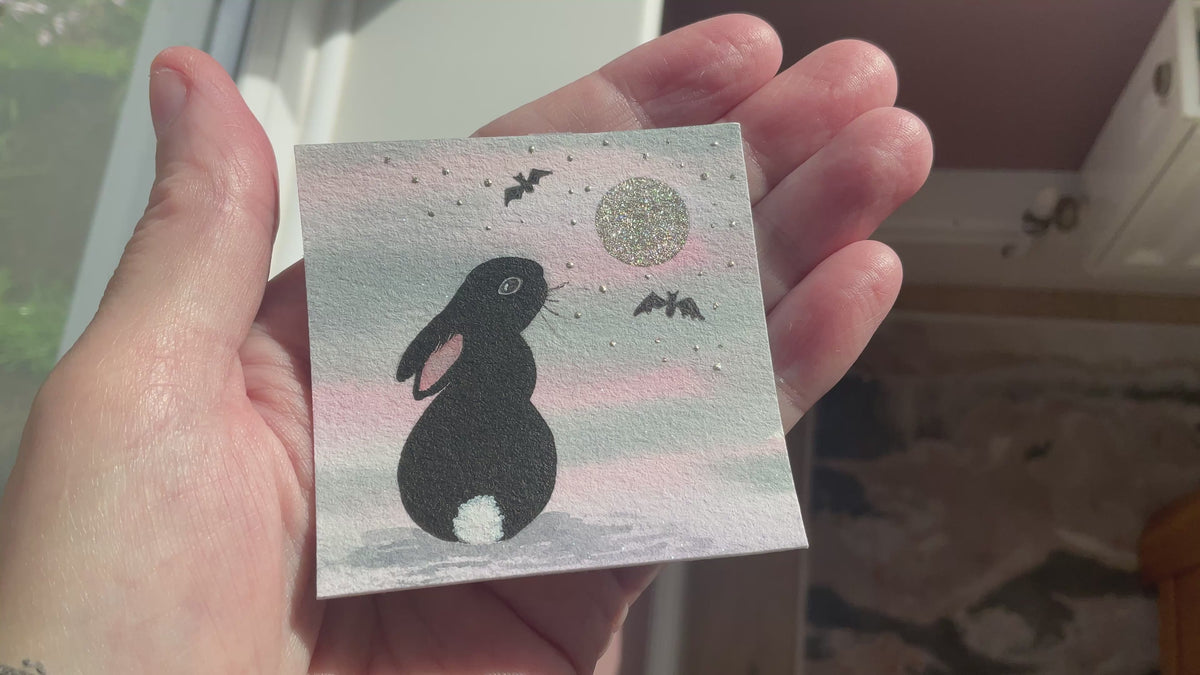 Video of Original mini watercolor painting titled Under the Silver Moon featuring a black rabbit silhouette looking up at a silver metallic moon and bats