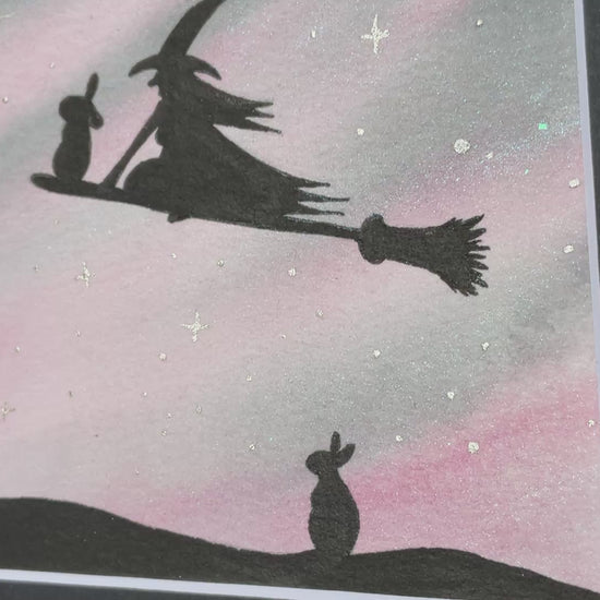 Video Original mini watercolor painting titled Waiting My Turn featuring a witch and a rabbit flying on a broomstick while a second rabbit waits on the ground under silver stars.