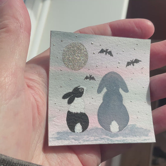 Video of Original mini watercolor painting titled Batty About You featuring two rabbit silhouettes sitting together under a metallic silver moon and bats.
