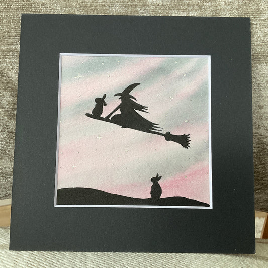 Original mini watercolor painting titled Waiting My Turn featuring a witch and a rabbit flying on a broomstick while a second rabbit waits on the ground under silver stars.